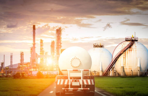 Tanker truck approaching a refinery and spherical storage tanks at sunset